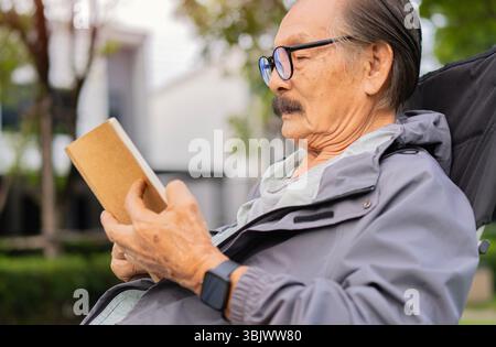 Side view of  mature senior old elderly man with grey hair , eyeglasses reading book at outdoor. Grandfather`s leisure activity on retired concept. Stock Photo
